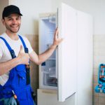 professional_young_repairman_worker_uniform_cap_with_modern_toolbox_with_equipment_after_repair_refrigerator_kitchen