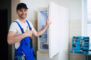 professional_young_repairman_worker_uniform_cap_with_modern_toolbox_with_equipment_after_repair_refrigerator_kitchen
